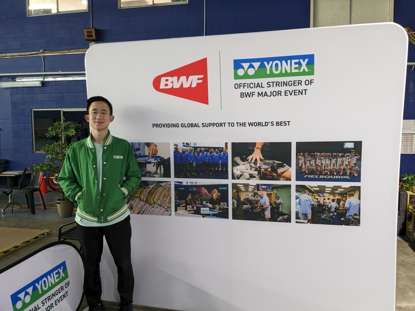 Erwin Tan standing in front of the BWF x Yonex 'Official Stringer of BWF Major Event' backdrop, his badminton stringing credential